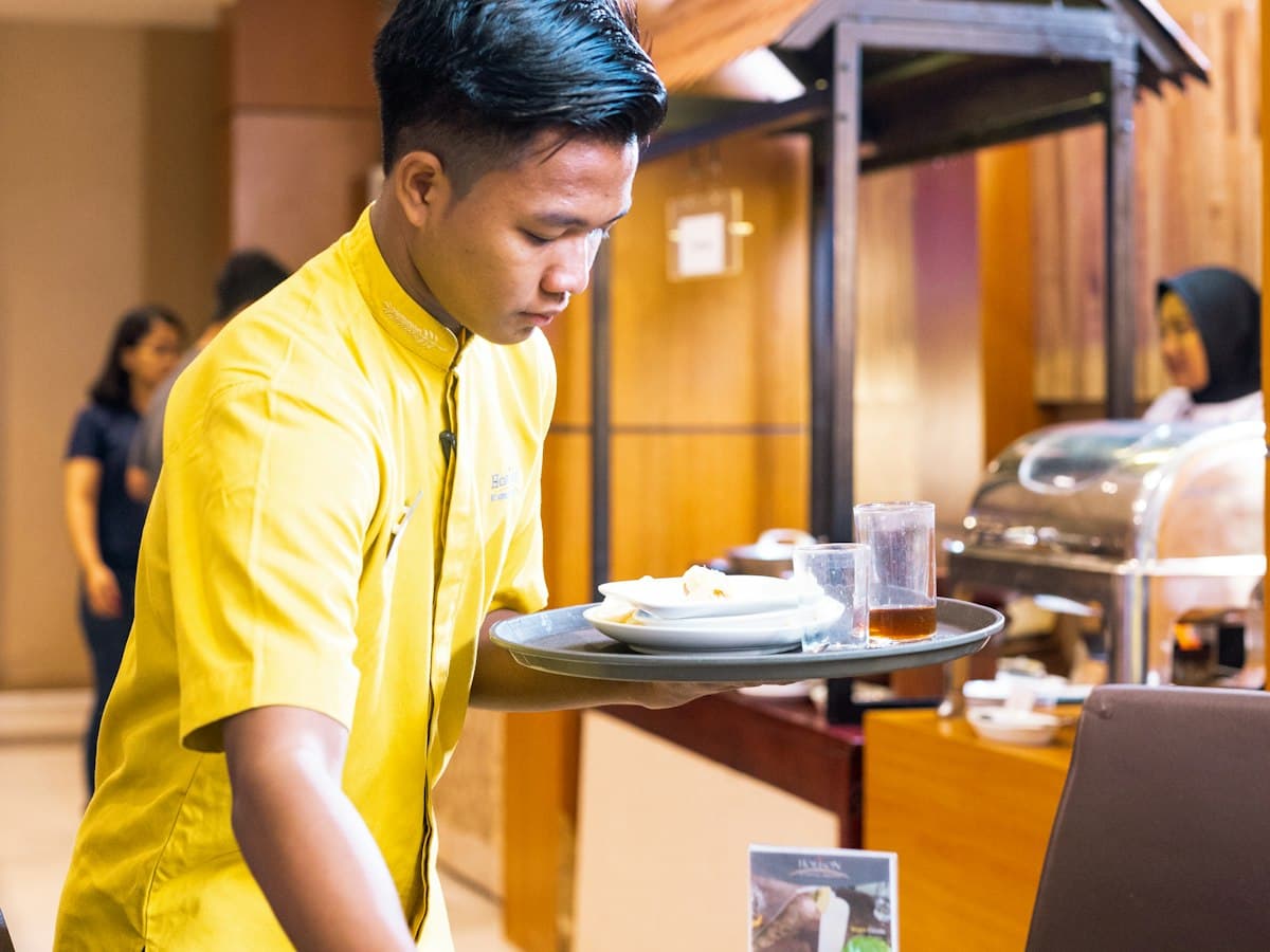 A hotel worker in a yellow uniform carrying a tray of dishes