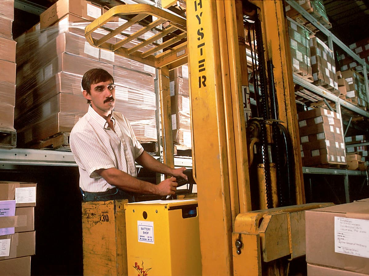 A warehouse worker operating a forklift among stacked boxes