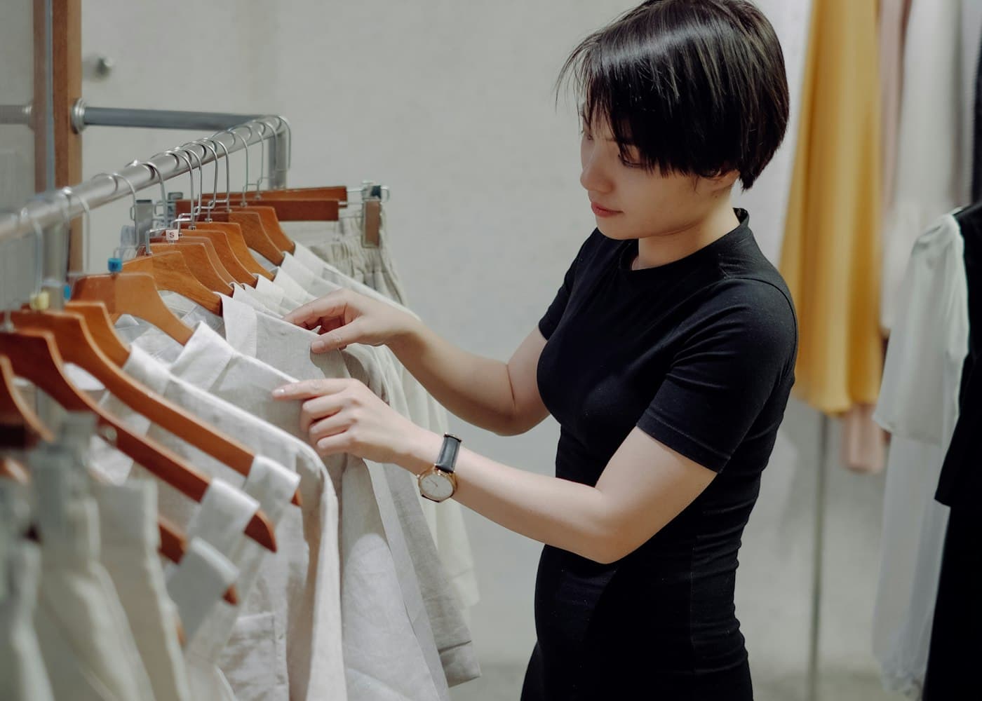 A woman shop assistant in a black top sorting white shirts on a clothes rail in a clean, bright shop