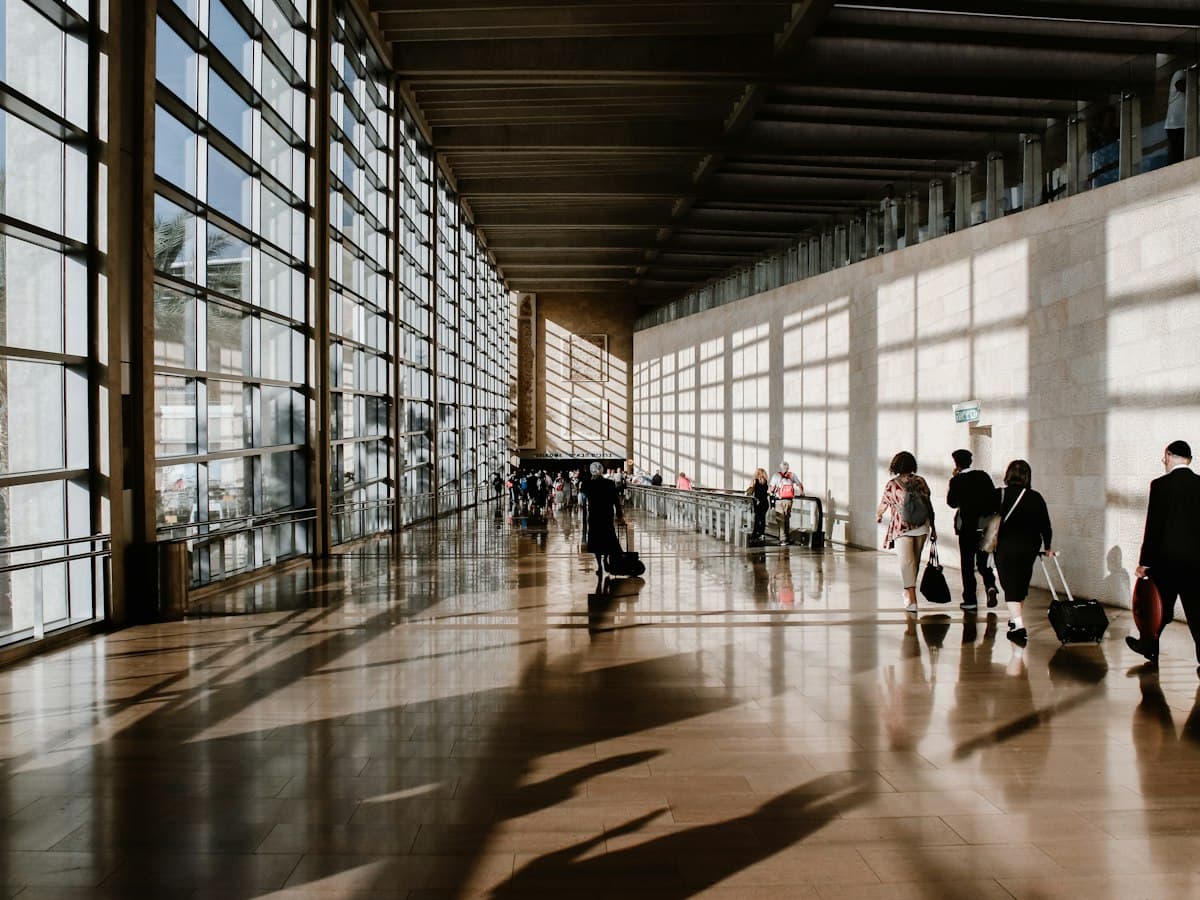 Travellers with suitcases walking through a sunlit airport terminal